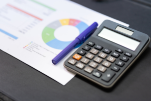 Calculator and pen on a desk with a financial chart in the background.