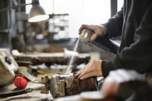 Spraying lubricant on a mechanical component in a workshop setting.