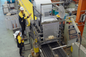 Workers operating a plastic wrapping machine in an industrial factory.